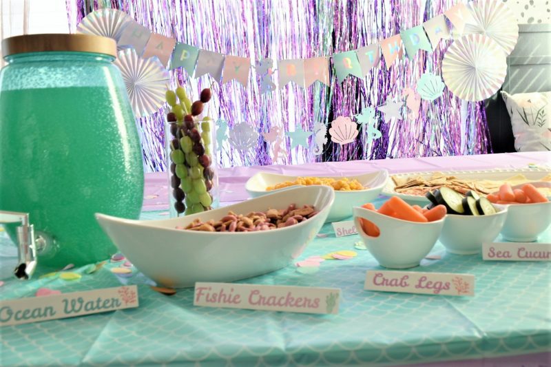 Mermaid birthday party food table with mermaid themed party decorations and backdrop