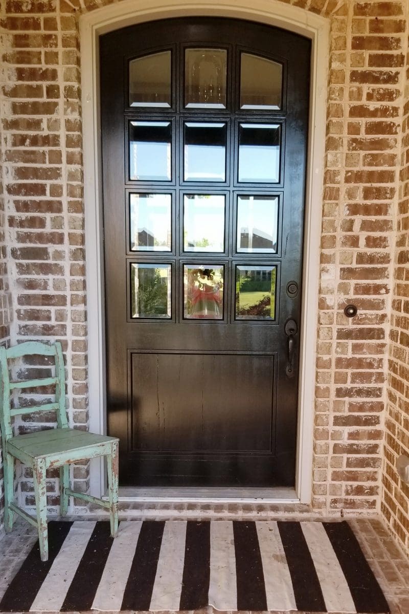 wooden front door of brick house with chippy green chair