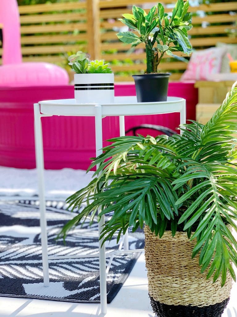 stock tank pool that is painted pink on a DIY deck Summer decor accents including tropical rug and tropical plants