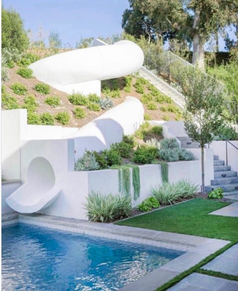 modern white pool slide on hill with stairs and landscaping